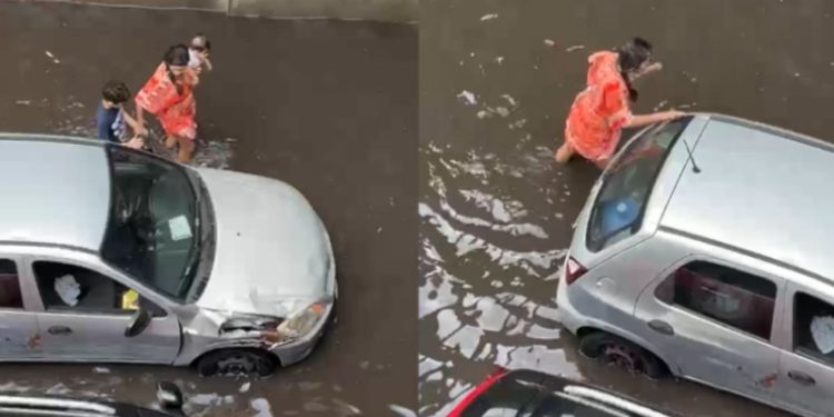 Após chuva, mãe com bebê no colo tenta empurrar carro na avenida Efigênio Sales